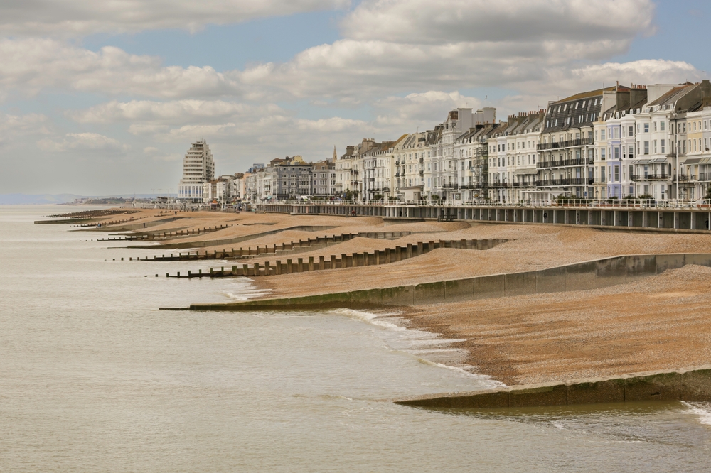 Groynes help trap sediment along eroding coastlines by interrupting longshore drift, extending the beach width over time. They are often combined with beach nourishment to maintain sediment levels in built-up coastal areas.
